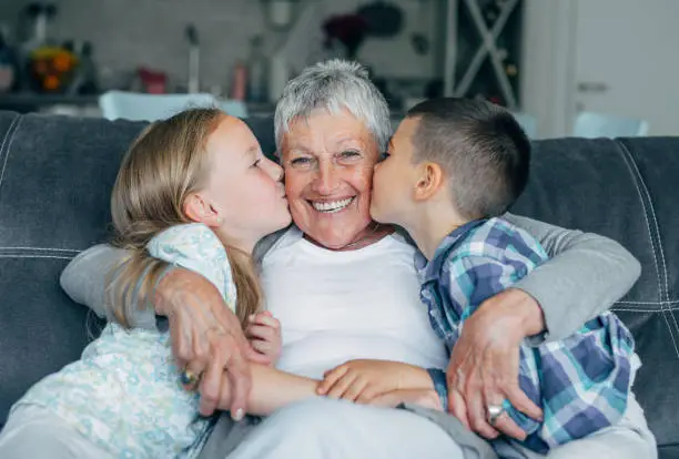 Grandmother embracing her cute grandson and granddaughter on the sofa at home.