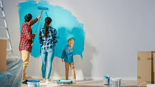 かわいい小さな娘と一緒に壁を描く若い家族の壁のバックショット。彼らはライトブルーの塗料で覆われているローラーでペイントします。自宅の部屋の改装。 - female house painter home decorator paintbrush ストックフォトと画像