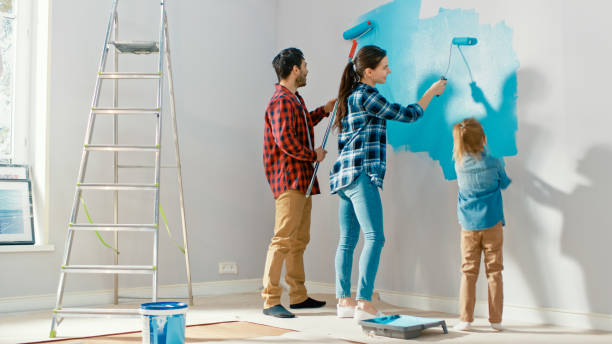 小さな娘と一緒に家族の時間。子供にローラーで壁を描く方法を示す若い父と母。ペイントカラーはライトブルーです。自宅の客室は改装工事の準備が整っています。 - female house painter home decorator paintbrush ストックフォトと画像