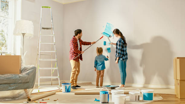 美しい若い家族は、彼らの愛らしい小さな娘に壁をペイントする方法を示しています。彼らはライトブルーの塗料で覆われているローラーでペイントします。自宅の部屋の改装。 - diy ストックフォトと画像