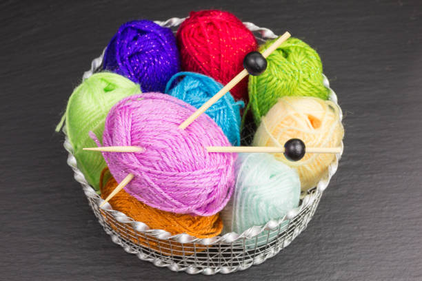 assortment of balls of wool in bright colors with knitting needles in a basket