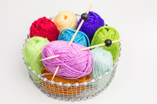 assortment of balls of wool in bright colors with knitting needles in a basket