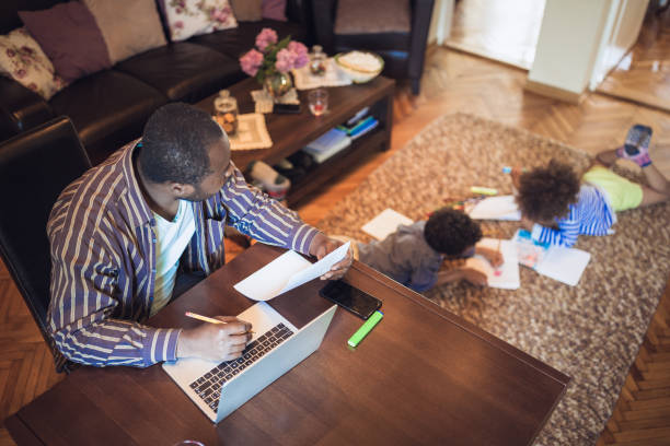 Father working from home Father working from home while his two children are playing in the living room single father stock pictures, royalty-free photos & images