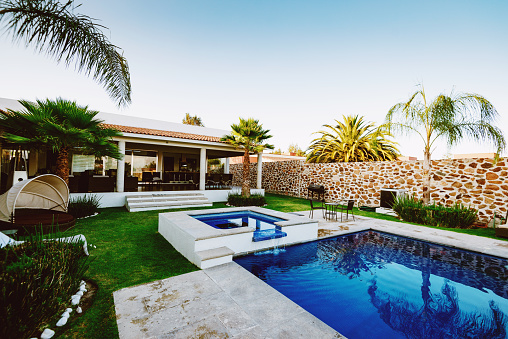 Luxurious long swimming pool overlooking the arid volcanic mountains, surrounded by a perfectly trimmed lawn, tranquil atmosphere of a high-end residential property suited for a lavishing lifestyle.
