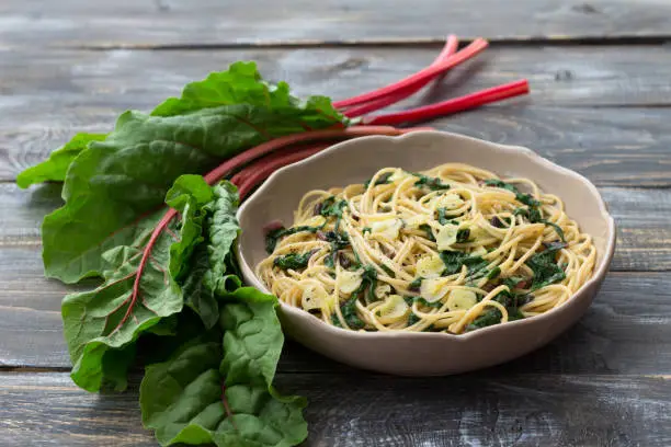 Vegan spaghetti with chard and garlic on a wooden table. Delicious homemade food