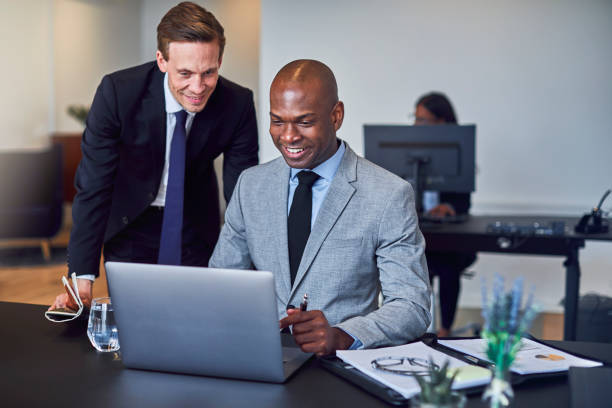 istock Two smiling diverse businessmen working on a laptop together 1156716448