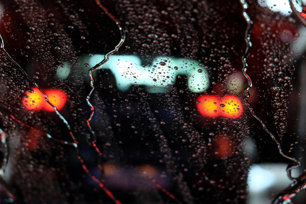 Car running through automatic carwash. Windscreen view from inside. Abstract wet windshield background. Red brake lights of car ahead. Wash conveyor