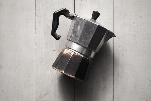 Old Italian moka pot lay on gray wooden table. It is a old stove-top coffee maker that brews coffee by passing boiling water pressurized by steam through ground coffee