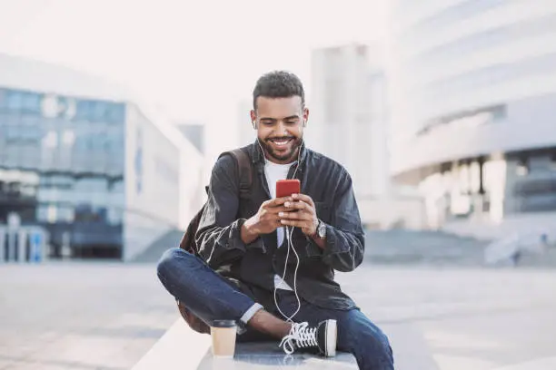 Photo of Cheerful young man using smart phone in a city