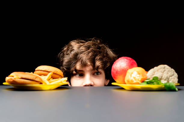 young male making choice between healthy vegetables or junk fast food b young male making choice between healthy vegetables or junk fast food overweight child stock pictures, royalty-free photos & images