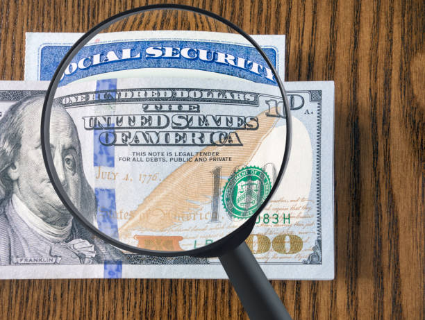 Dollar bills and Social Security Card Looking down on a pile of 100 dollar bills and Social security card with magnifying glass social security social security card identity us currency stock pictures, royalty-free photos & images