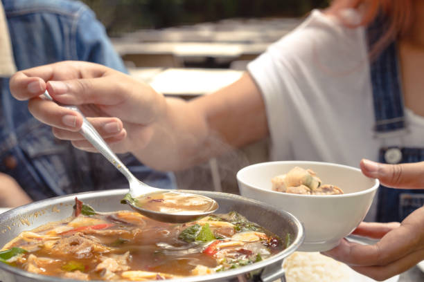 Hand serving hot Asian soup into a bowl during a family dinner meal at a restaurant stock photo