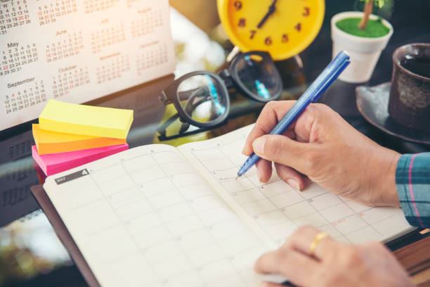 na página do calendário 2019, planejador de mão fêmea ou organizador que escreve a nomeação diária. marca da mulher e programação anotada (desengate do feriado) no livro ou no diário na mesa de escritório. evento do lembrete do calendário para  - calendar page book personal organizer - fotografias e filmes do acervo