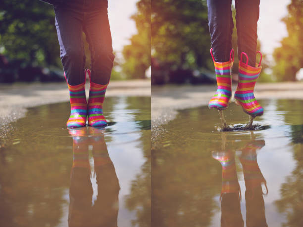 Close-up of a little girl's boots and umbrella reflecting in a rain puddle.