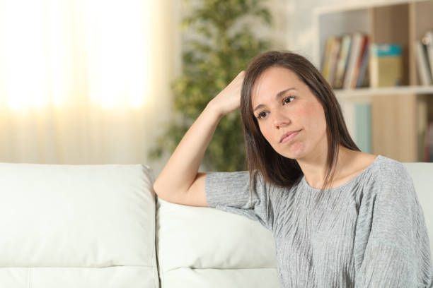 istock Pensive woman looking away on a couch at home 1156733713