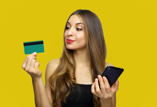 giovane donna con carta di credito shopping online mentre si utilizza il telefono cellulare su sfondo giallo - showing buying paying clipping path foto e immagini stock