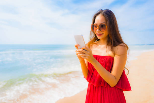 istock Young Woman Using Mobile Phone While Standing At Beach Against Sky 1156741778