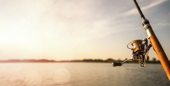 Close up of a fishing rod during the sunset at the lake with copy space