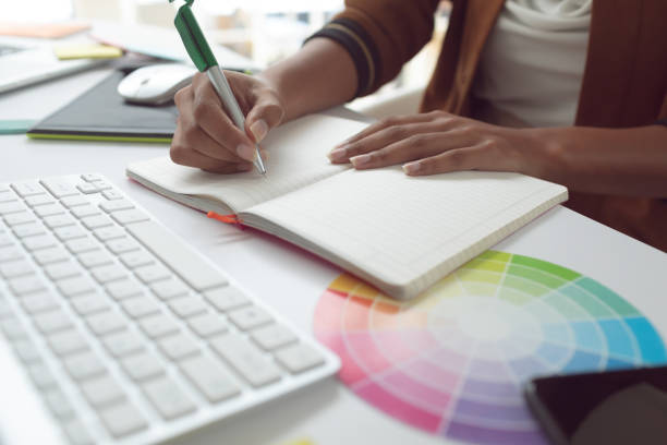 istock Female graphic designer writing on diary at desk in a modern office 1156748840