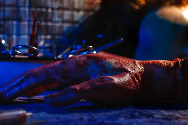 A severed hand in blood and part of heads lie on the table. Staged photo with a creepy and gloomy atmosphere. The concept of murder and dismemberment of the victim