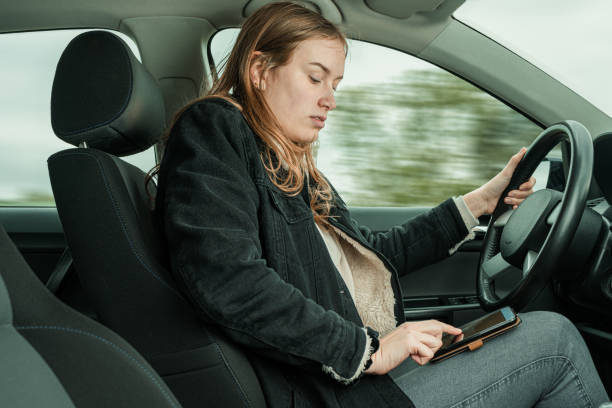 una mujer escribe un mensaje en su smartphone mientras conduce un coche - careless fotografías e imágenes de stock