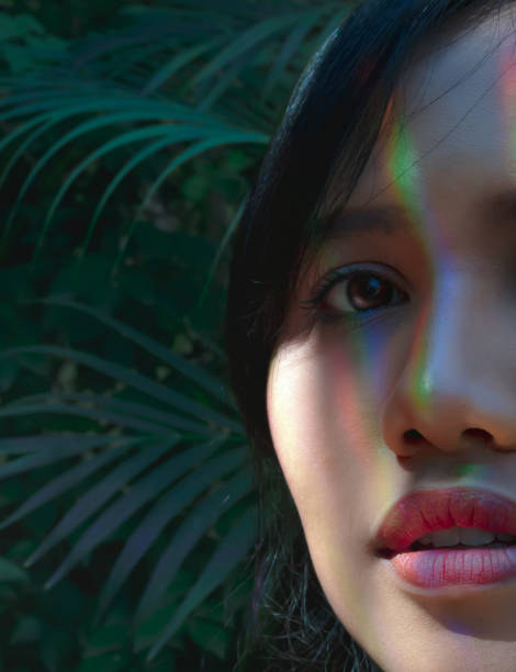 istock Ethnic Asian girl half face portrait in a rainforest with rainbow multicoloured refracted light shining on her head 1156753745