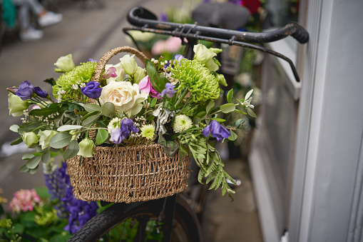 Detail of a parked vintage black bicycle with a bunch of fresh flowers in the front wooden basket. Landscape format.
