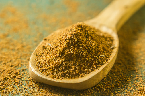 Many colorful, organic, dried, vibrant Indian food, ingredient spices in small aluminum metal spice scoops are arranged in a circle on an old blue-colored ceramic plate background, sitting on a vibrant, colorful contrasting textile. Very shallow depth of field, good copy space in the center of the image.