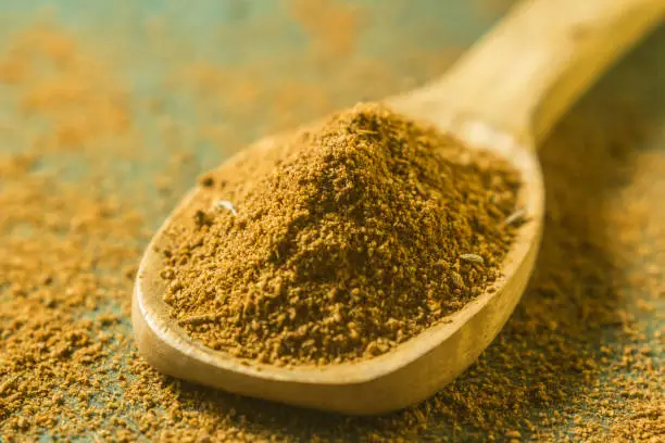 Photo of Ground cumin powder in wooden spoon.