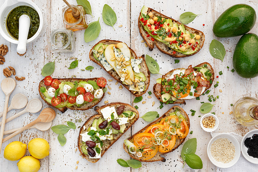Variation open faced sandwiches, Open avocado sandwiches made of  slices of sourdough bread with  various toppings on a white wooden table, top view