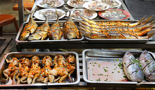 Traditional asian night market with delicious seafood and exotic food for tourist. Marinated fish and frogs on the counter of a street restaurant for grilling. Night photo under fluorescent light