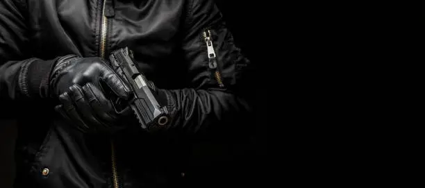 a man in a black jacket and black gloves holding a gun on a dark background