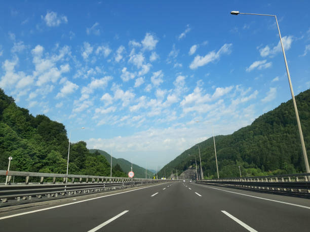 istock Road trip, green forests and highway, blue sky through car windscreen 1156778017