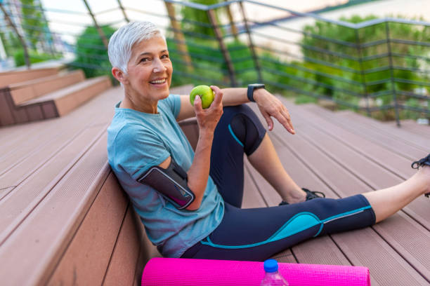 Mature athletic woman eating an apple after sports training Sporty woman eating apple. Beautiful woman with gray hair in the early sixties relaxing after sport training. Healthy Age. Mature athletic woman eating an apple after sports training apple bite stock pictures, royalty-free photos & images