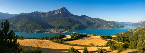 panoramic du lac serre-poncon avec le village de savines-le-lac et champs de blé à la lumière du matin d'été. alpes européennes, provence-alpes-côte d'azur. hautes-alpes (05), savines-le-lac - france european alps provence alpes cote dazur mountain photos et images de collection