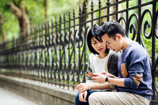 Asian couple looking at smartphone on park wall