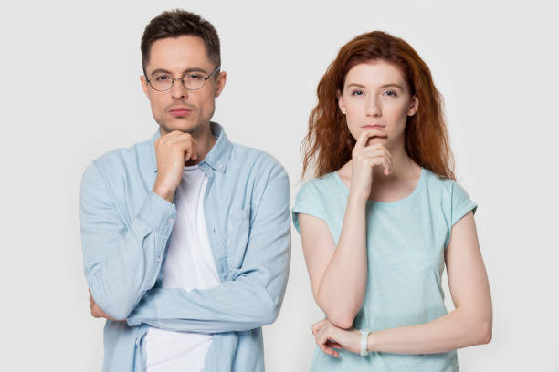 Pensive couple touch chin with finger thinking of something Pensive millennial couple stand isolated on grey studio background touch chin with finger thinking of something, thoughtful man and woman consider or plan idea, look at camera lost in thoughts two people thinking stock pictures, royalty-free photos & images