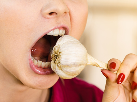 Crazy young woman having fun eating garlic vegetable. Healthy food, fighting disease concept.