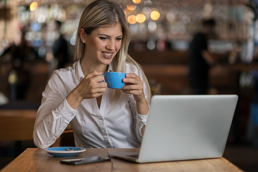 Young happy businesswoman reading an e-mail on laptop in a cafe