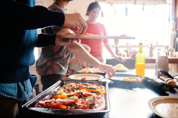 Millenial multi-ethnic roommates cooking vegetalian, vegan pizza stock photo