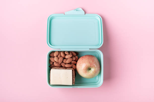 Lunch box with apple, sandwich and almond on pink background Back to school concept with copy space for text stock photo