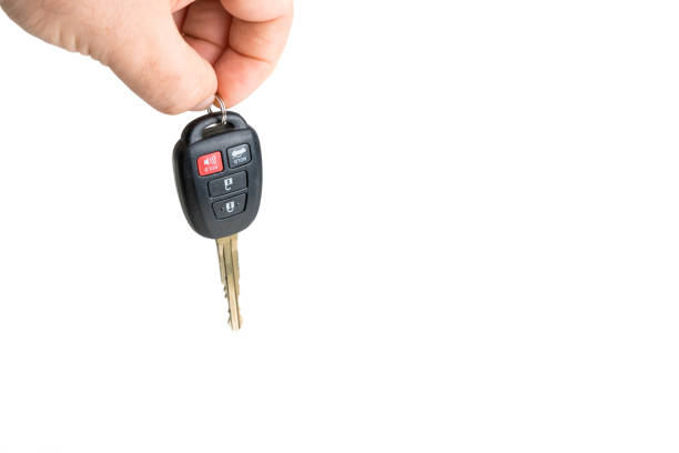 A male is dangling a Toyota car key with the locking buttons visible. Only the fingers of the males hand are visible. The background is white.