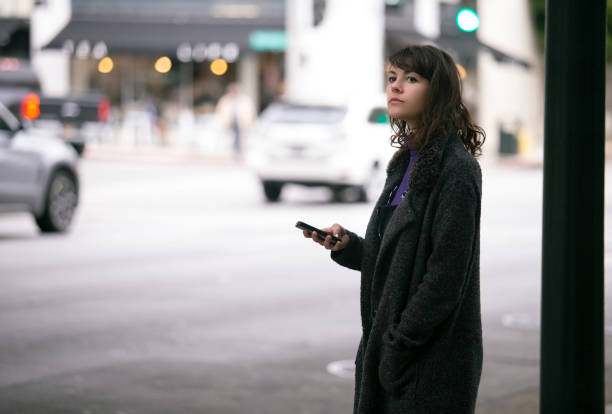 female pedestrian waiting with cellphone for a ride share - chamada de fotografia imagens e fotografias de stock