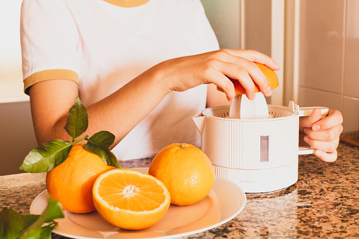 Detail of a teen's hands holding a citrus juicer with orange half and freshly squeezed citrus.