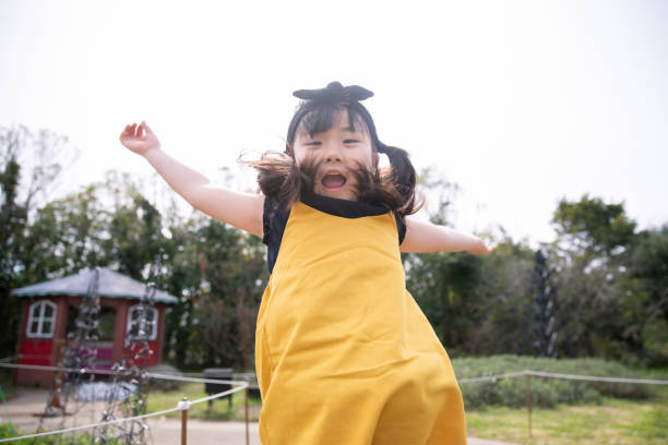 bambina che salta nel parco pubblico - arms raised green jumping hand raised foto e immagini stock