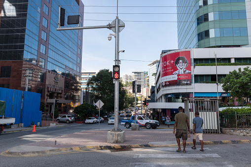 Two men cross a street in Port Moresby, Papua New Guinea. An advertisement for Digicel is on a building before them. (June 14, 2019)