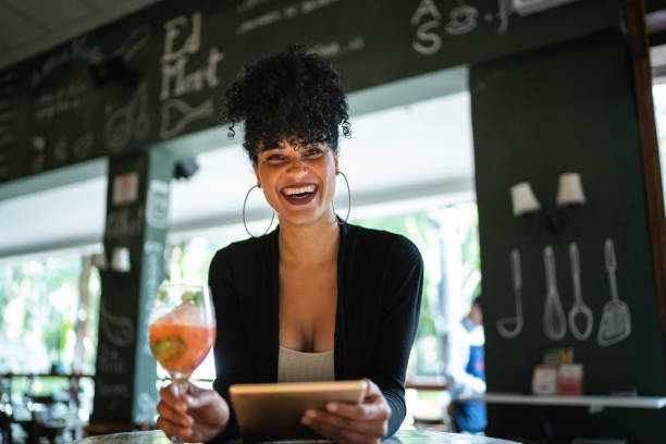 バーでデジタルタブレットを飲んで使用する笑顔の女性の肖像画 - cocktail bar caipirinha drink ストックフォトと画像