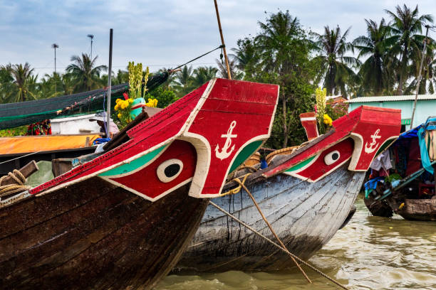 Boats with eyes and anchor painting decoration on the prow, anchored in the muddy waters of the Mekong Delta, Vietnam. stock photo