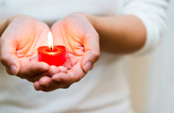 istock Woman hands holding burning heart-shaped candle 1156845295