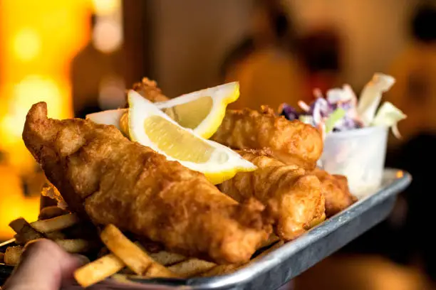 Holding a plate of Fish and Chips with coleslaw and fries